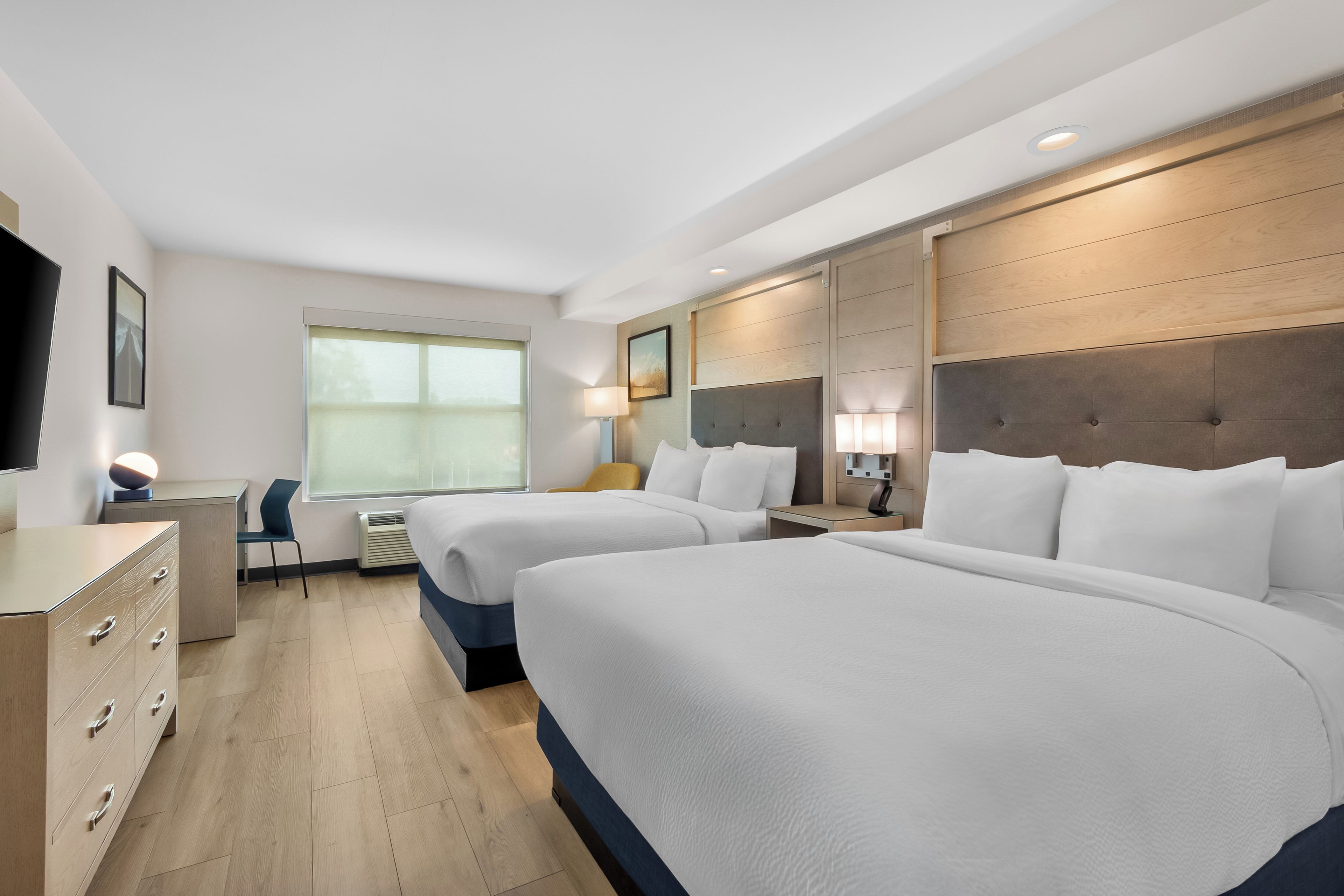A hotel room with two beds, a desk, a chair, a TV, and a window.