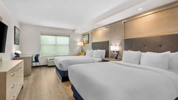 A hotel room with two beds, a desk, a chair, a TV, and a window.