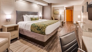 Ein modernes Hotelzimmer mit einem großen Bett, Nachttischen, einem Schreibtisch, einem Sessel und einem Kleiderschrank.