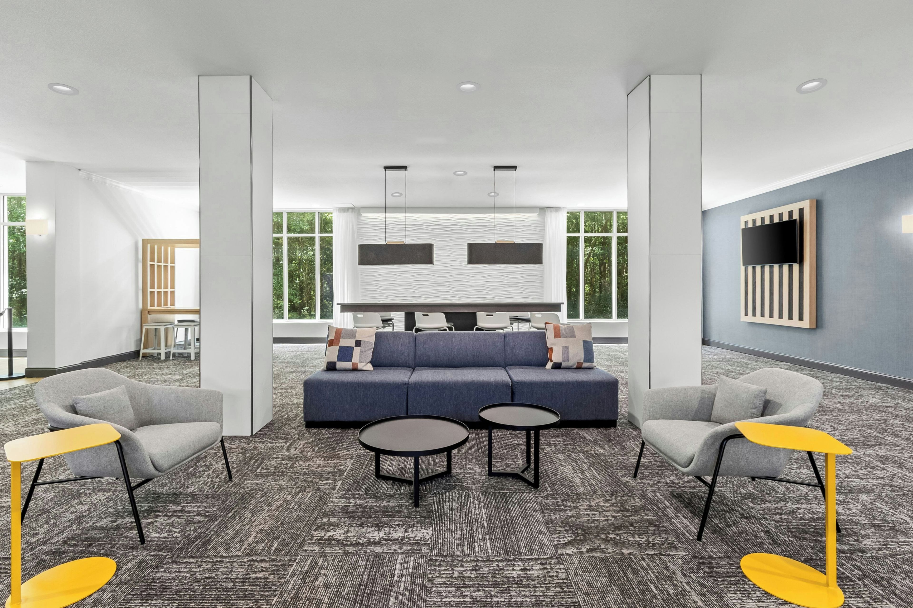 A modern lounge area with a sofa, armchairs, and a coffee table, featuring a patterned carpet and large windows.