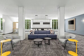A modern lounge area with a sofa, armchairs, and a coffee table, featuring a patterned carpet and large windows. - City Express by Marriott Pooler Savannah Airport (Pooler)