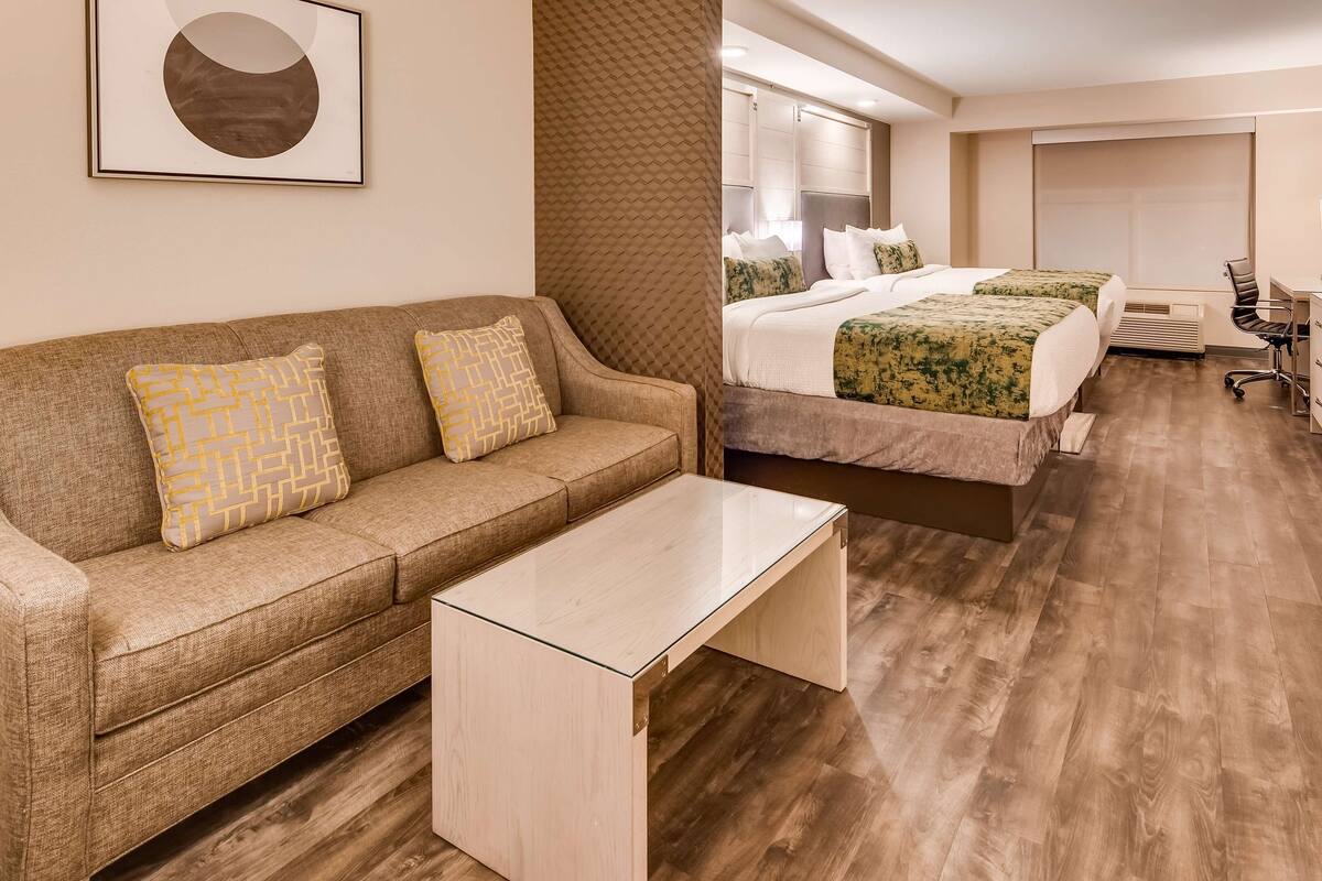 Une chambre d’hôtel avec un canapé, deux lits, un bureau, une chaise et un téléviseur.