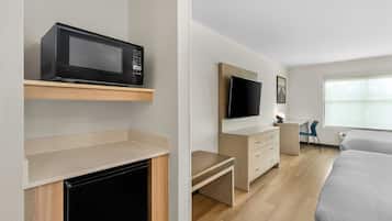 Une chambre d’hôtel moderne équipée d’un téléviseur à écran plat fixé au mur, d’un four à micro-ondes posé sur une étagère, d’un petit bureau avec des tiroirs et d’un lit recouvert d’une couette grise.