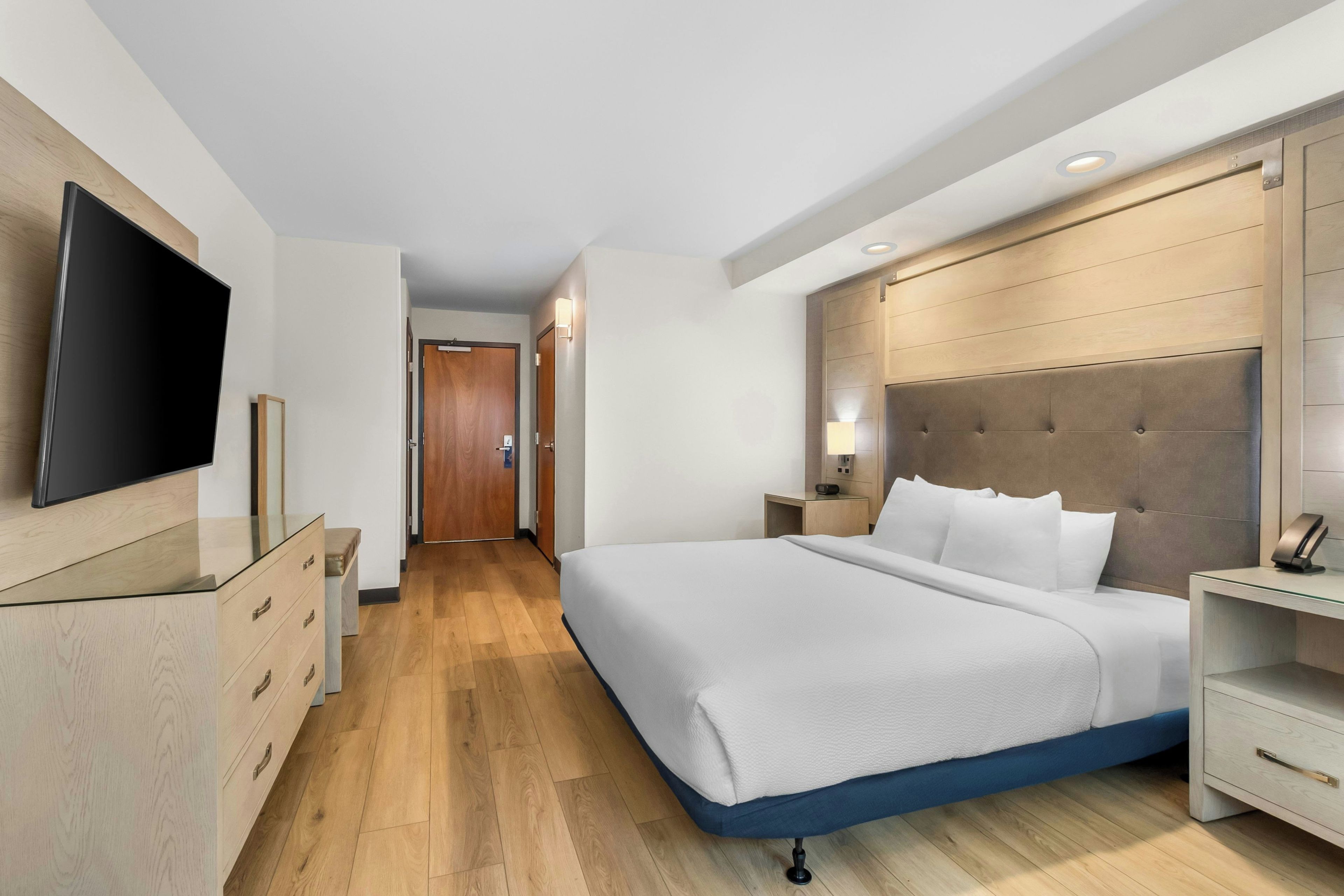 Habitación de hotel con una cama grande, mesitas de noche, un televisor de pantalla plana y un cabecero de madera.