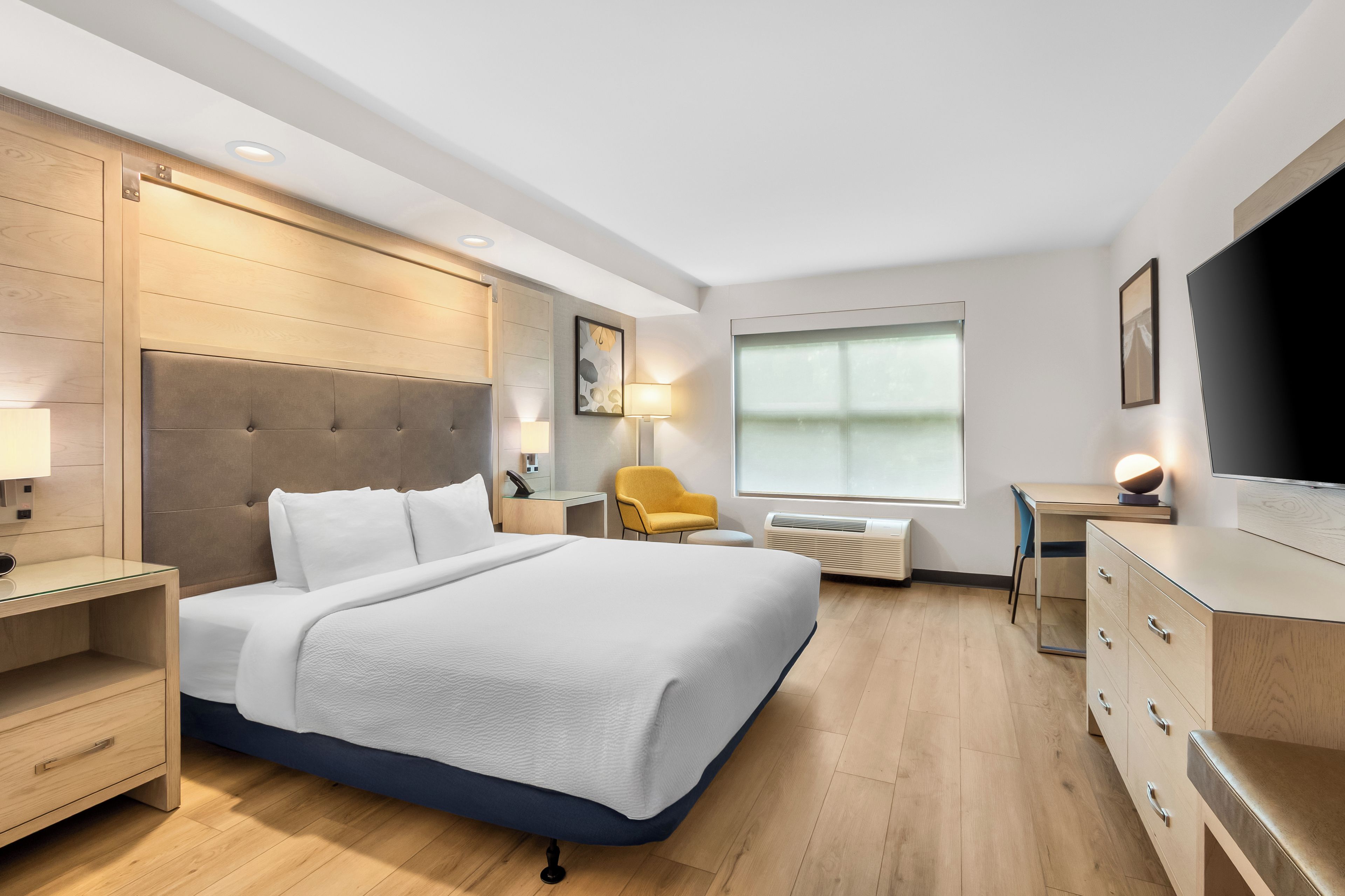 A modern hotel room with a large bed, bedside tables, a desk, a chair, a TV, and a window.
