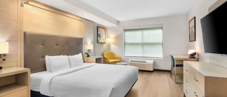 A modern hotel room with a large bed, bedside tables, a desk, a chair, a TV, and a window.