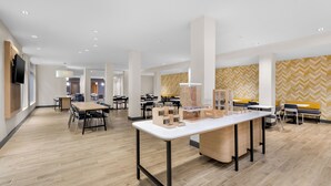 A spacious, modern interior with multiple seating areas, a central table with storage boxes, and a patterned wall in the background. - City Express by Marriott Pooler Savannah Airport (Pooler)
