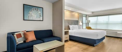 Une chambre d’hôtel avec un lit, un canapé, une petite table, une table de chevet, une lampe et une grande fenêtre.