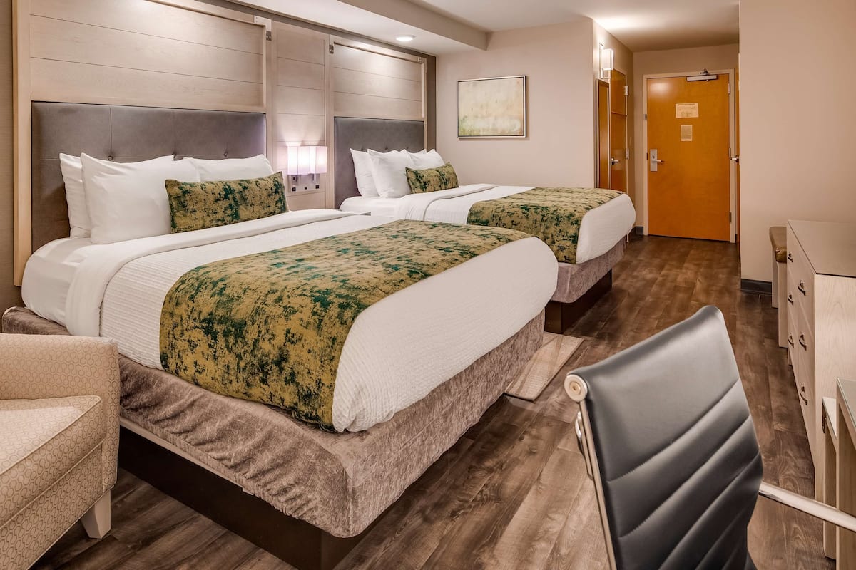 A hotel room with two beds, a desk, a chair, and a door.