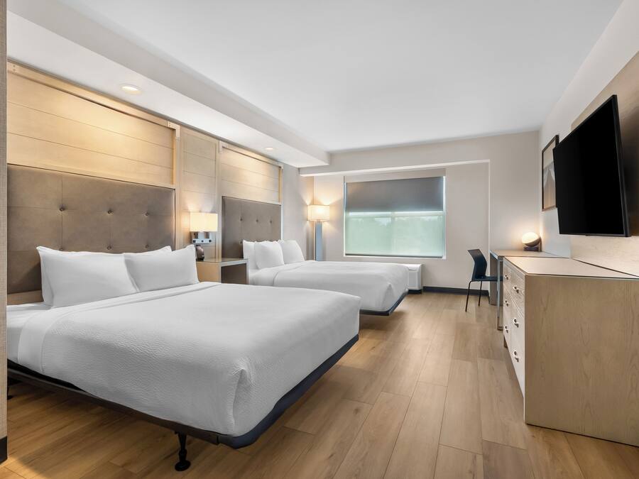 Habitación de hotel con dos camas, un escritorio, un televisor y una ventana.