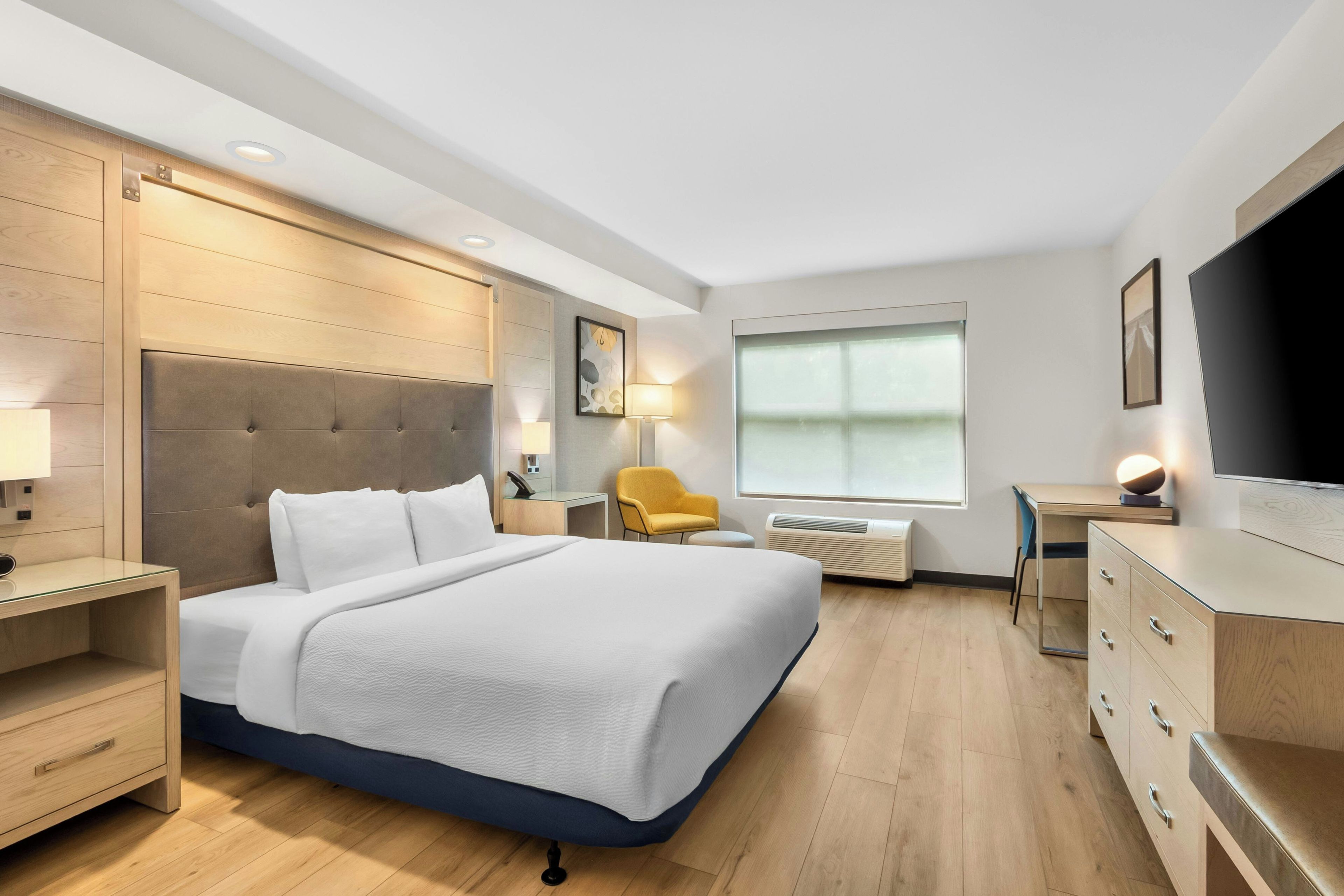 Habitación de hotel con una cama grande, mesitas de noche, un escritorio, una silla, un televisor y una ventana.