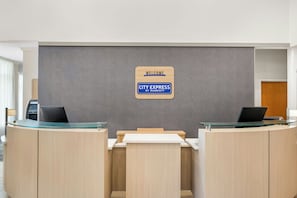 A reception desk with a 'WELCOME CITY EXPRESS BY MARRIOTT' sign, two laptops, and a glass-top table.