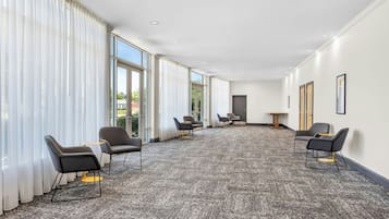 Amplia habitación con ventanas grandes, piso alfombrado y varias sillas dispuestas para sentarse.