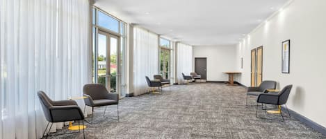 Amplia habitación con ventanas grandes, piso alfombrado y varias sillas dispuestas para sentarse.