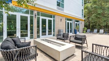 An outdoor seating area with a fire feature, cushioned chairs, and a modern building facade.
