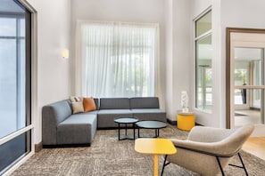 A modern living room with a sectional sofa, two small tables, a yellow side table, and a large window with sheer curtains.