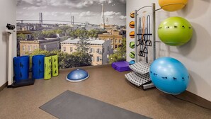 Ein Fitnessraum mit Trainingsgeräten, einer Stadtansicht als Wandgemälde und Blick auf Gebäude.