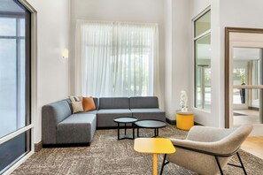 A modern living room with a grey sectional sofa, two small round tables, a yellow side table, and a grey armchair. - City Express by Marriott Pooler Savannah Airport (Pooler)