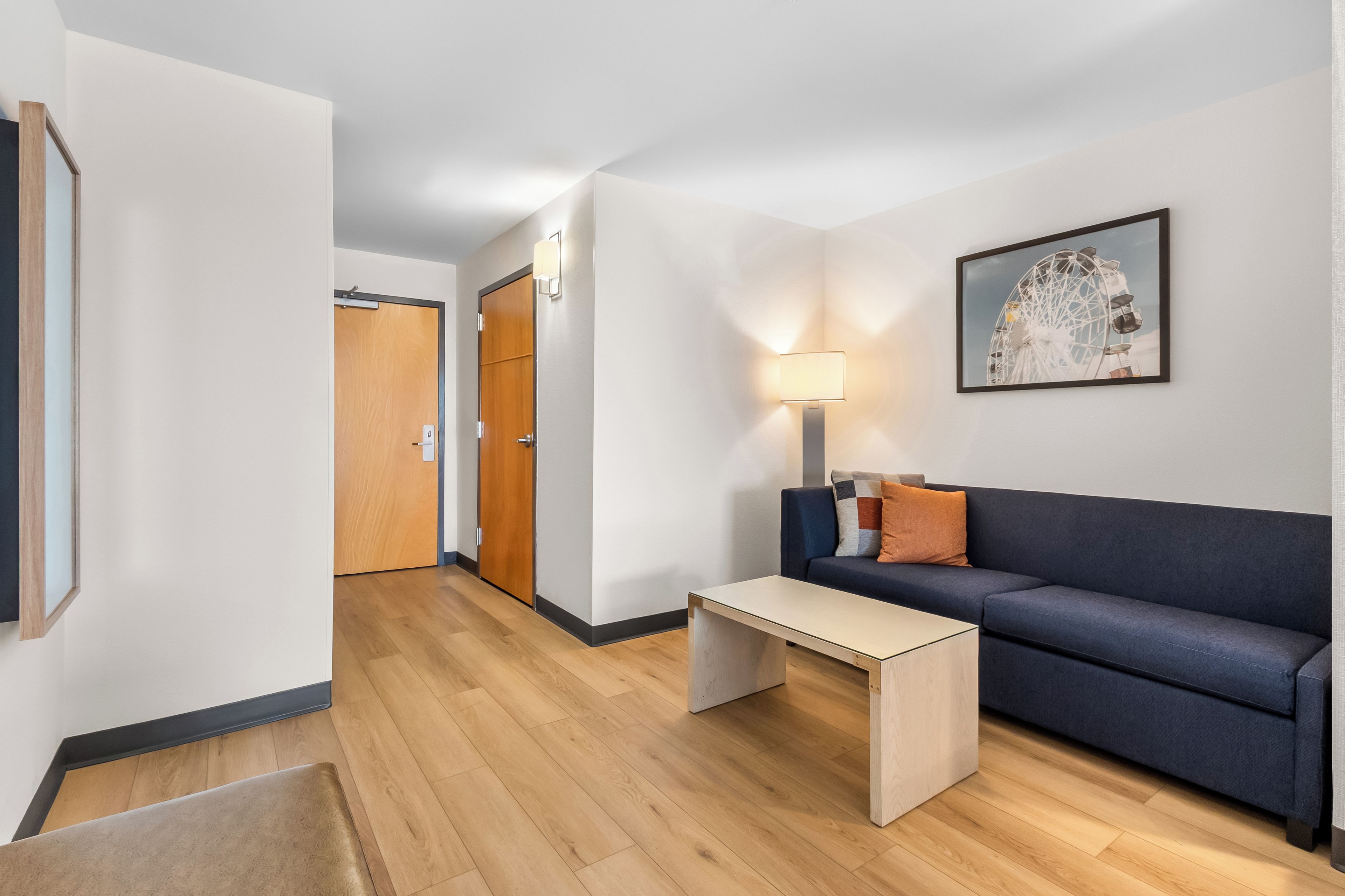 Habitación de hotel moderna con piso de madera, un sofá, una mesa de centro, una lámpara y un cuadro en la pared.