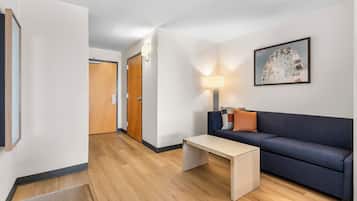 Habitación de hotel moderna con piso de madera, un sofá, una mesa de centro, una lámpara y un cuadro en la pared.