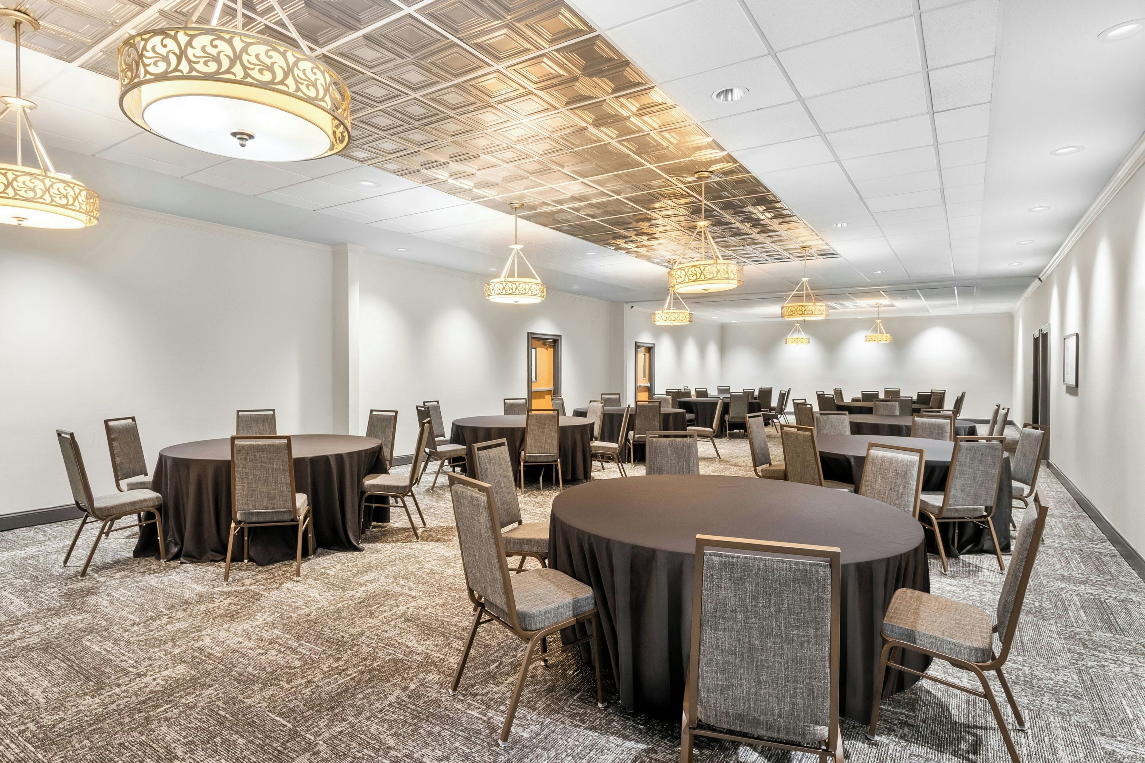 A conference room with multiple tables and chairs, a patterned carpet, and decorative ceiling lights.