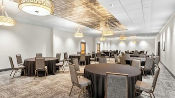 A conference room with multiple tables and chairs, a patterned carpet, and decorative ceiling lights.