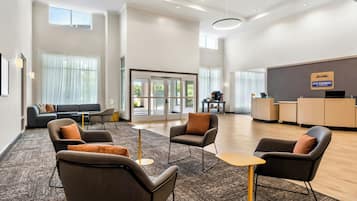 Un vestíbulo de hotel con una recepción, zona de estar con sofás y sillones, y ventanas amplias.