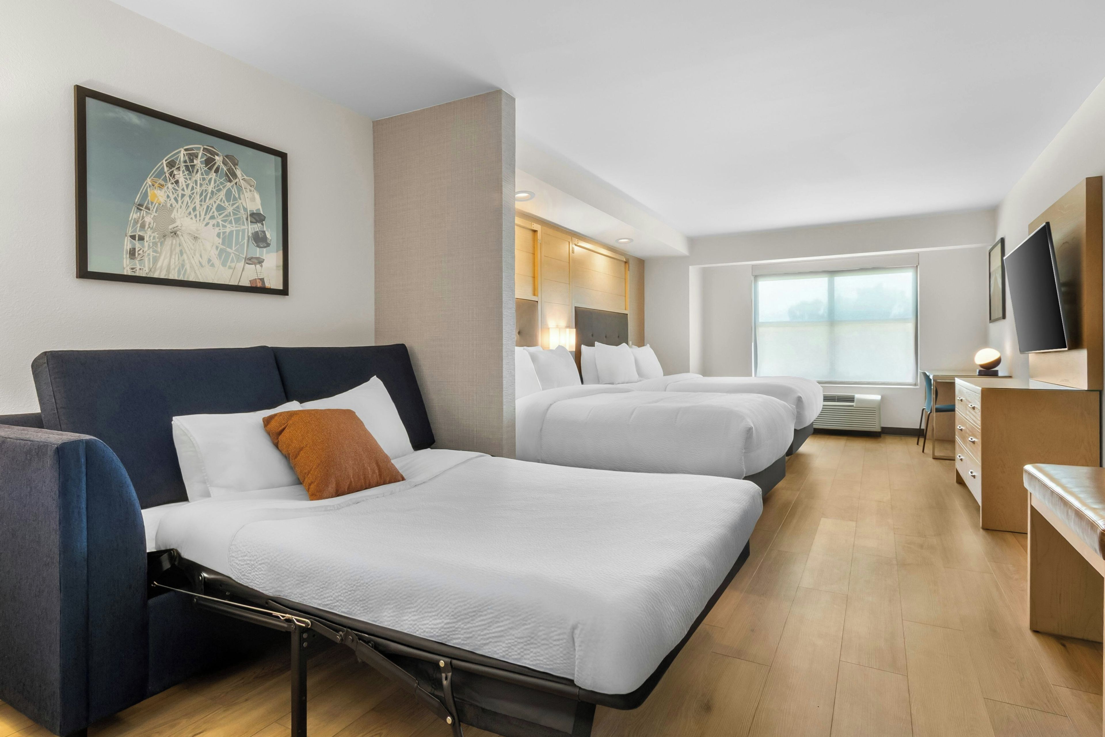 A hotel room with two beds, a sofa, a TV, and a large window.