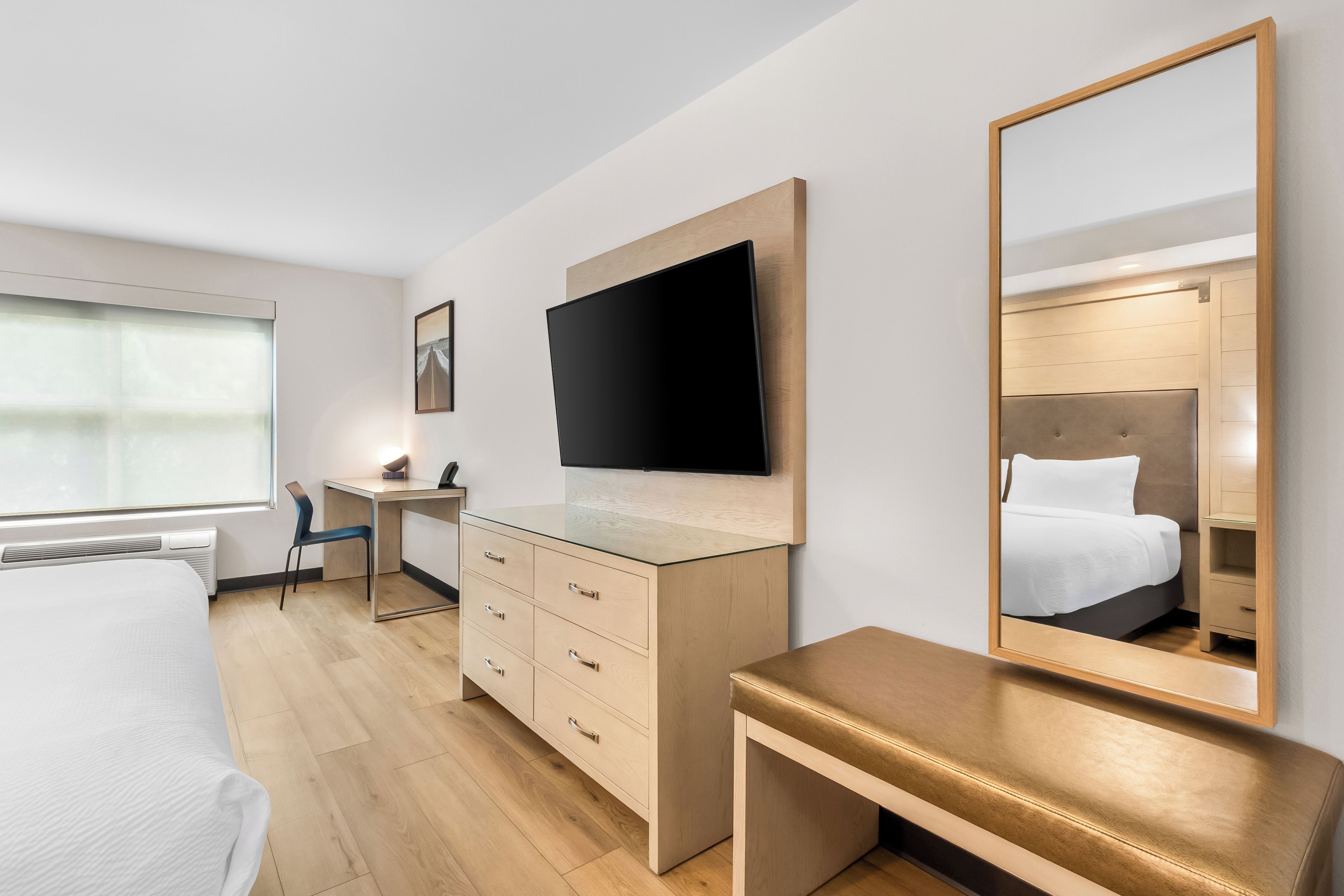 Une chambre d’hôtel équipée d’un lit, d’un bureau, d’une commode, d’une télévision et d’un grand miroir.