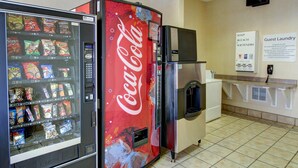 En automat med snacks og en Coca-Cola maskine. Skilt for gæstevaskeri og et køleskab.
