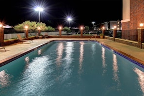 A nighttime swimming pool area with a brick wall, a fence, and outdoor seating. - Holiday Inn Express Hotel & Suites San Angelo by IHG (San Angelo)