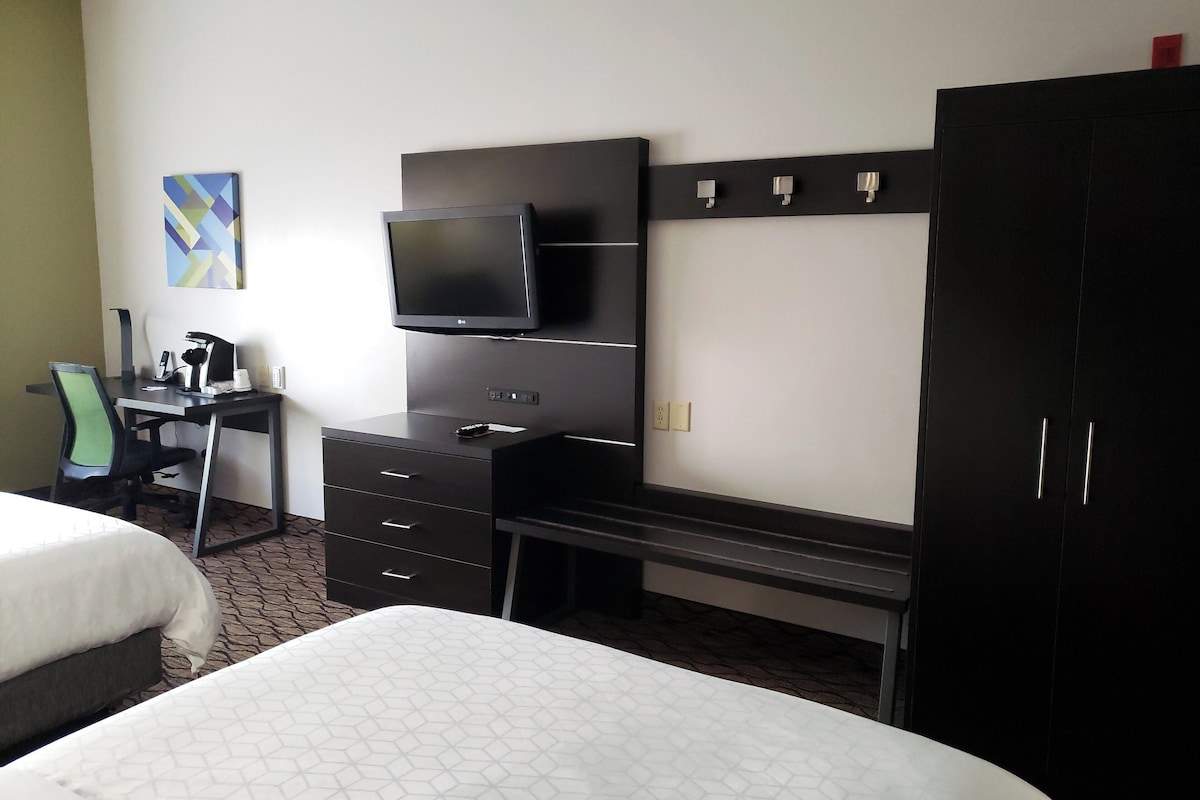 A hotel room with a bed, a desk with a computer and phone, a TV, and a wardrobe.