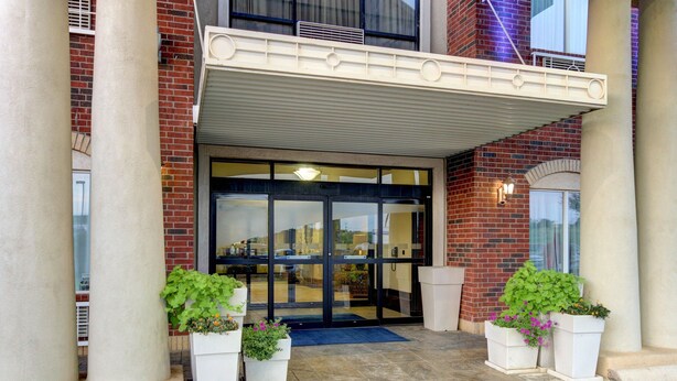 A hotel entrance with a glass door, large columns, and potted plants. - Holiday Inn Express Hotel & Suites San Angelo by IHG (San Angelo)