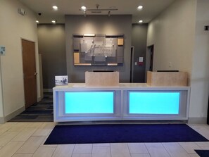 A reception desk with a digital display, a sign for Holiday Inn Express, and a security camera on the wall. - Holiday Inn Express Hotel & Suites San Angelo by IHG (San Angelo)