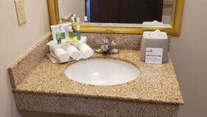 Et badeværelsesvask med toiletartikler, et spejl og en tissueske.
