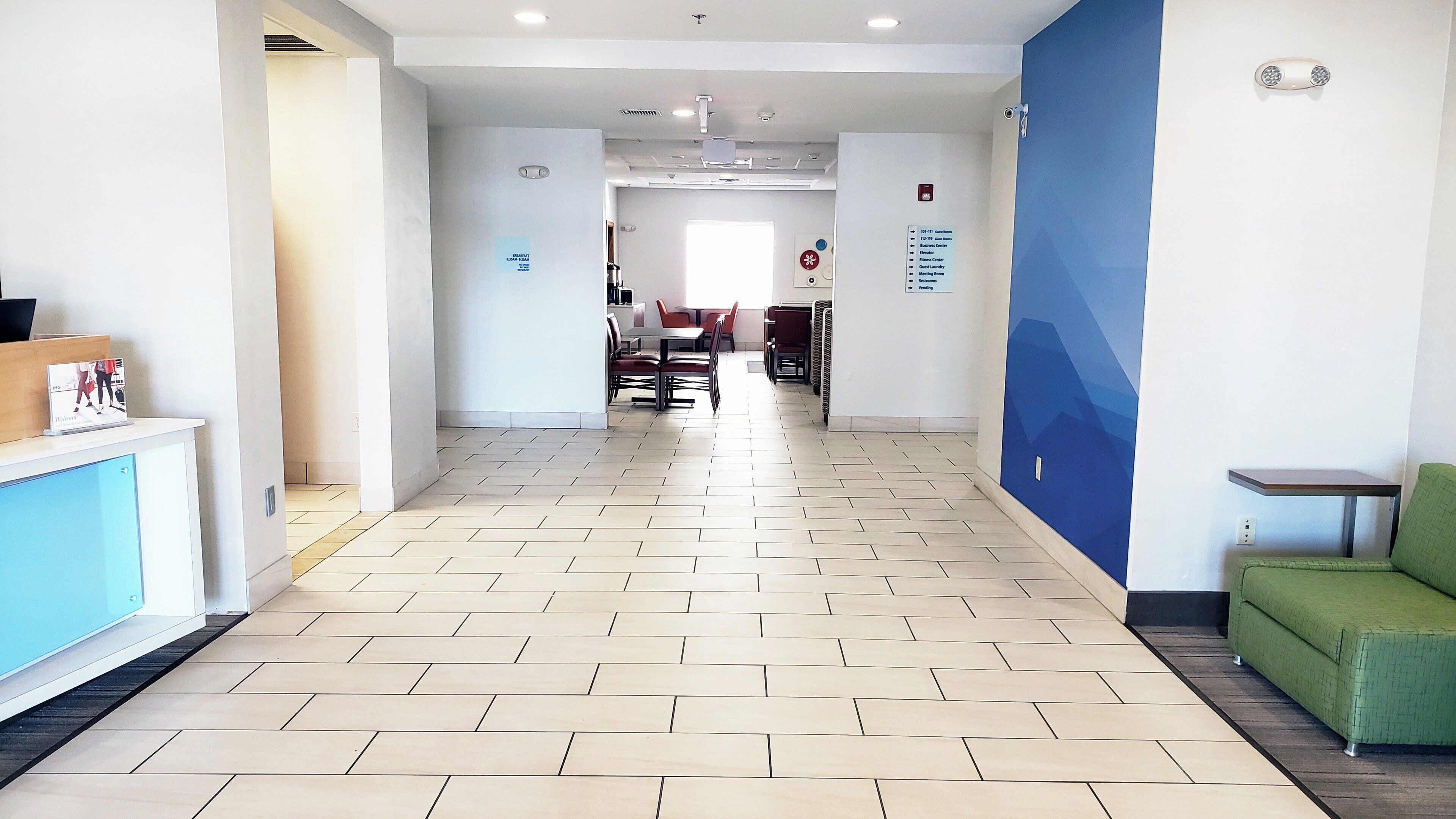 Un pasillo de hotel con mostrador de recepción, comedor y una zona de estar verde.