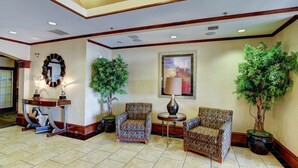 A lobby with two patterned armchairs, a small round table with a lamp, a potted plant, and a decorative mirror. - Holiday Inn Express Hotel & Suites San Angelo by IHG (San Angelo)