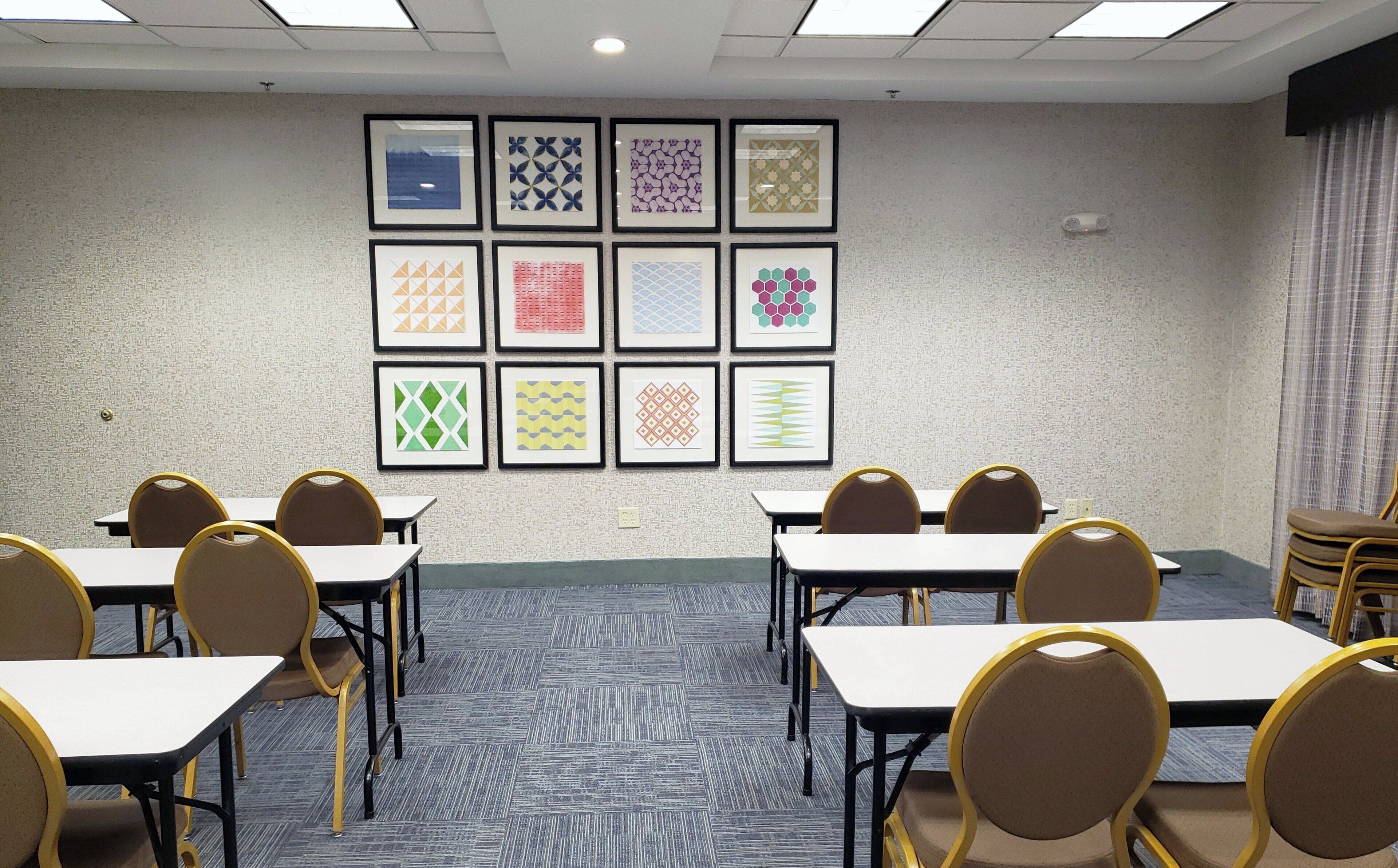Un salón de conferencias con mesas y sillas, una alfombra estampada y obras de arte enmarcadas en la pared.