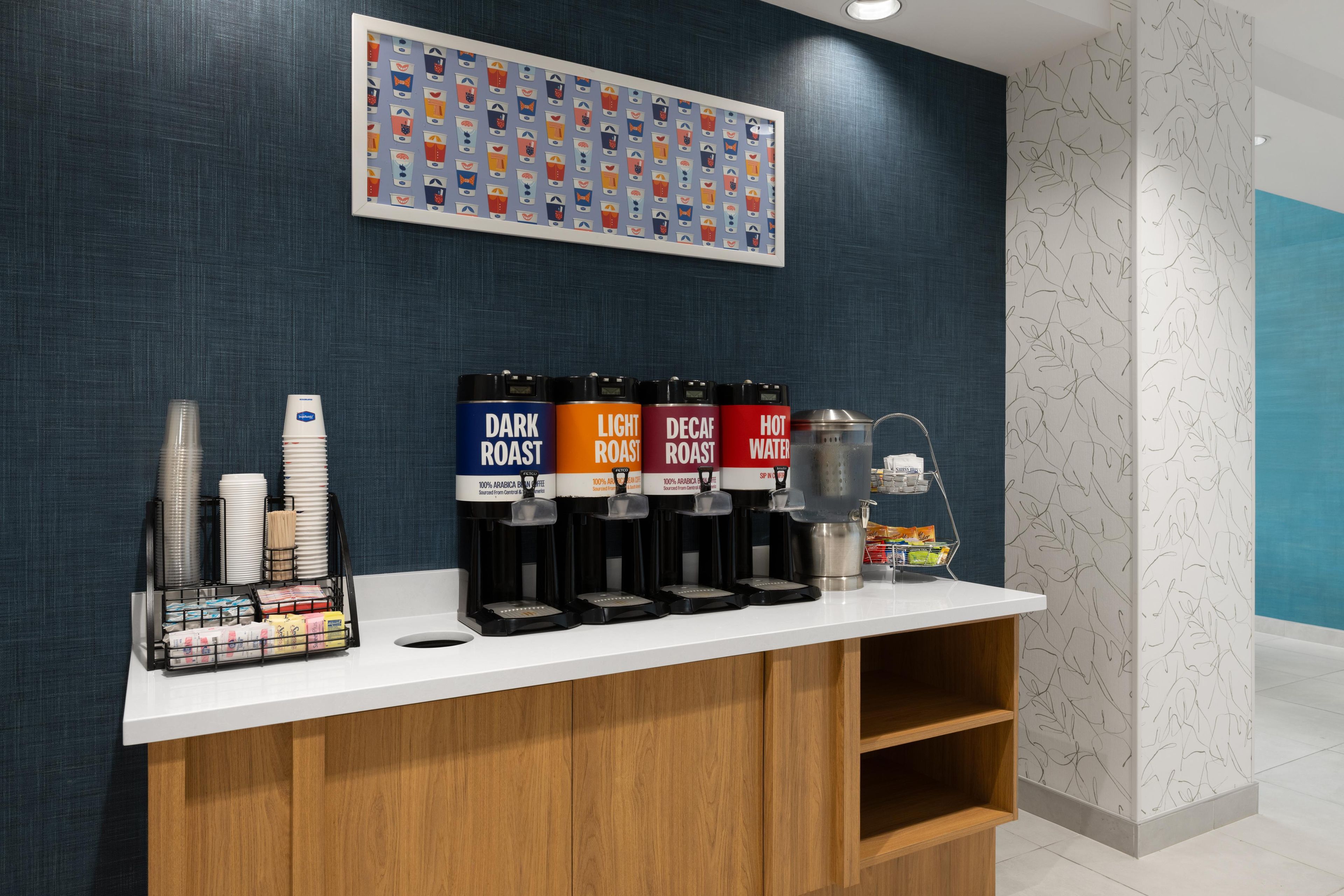 A coffee station with four dispensers labeled DARK ROAST, LIGHT ROAST, DECAF ROAST, and HOT WATER.