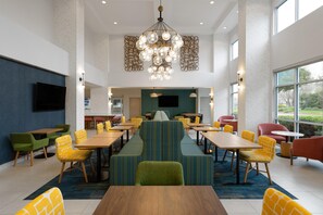 A spacious dining area with multiple tables and chairs, a central sofa, and a chandelier. - Hampton Inn & Suites Sacramento-Airport-Natomas (Sacramento)