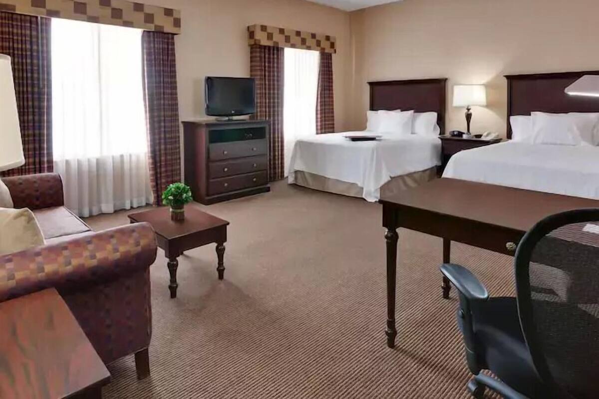 A hotel room with two beds, a TV, a desk, a chair, a lamp, and a dresser.