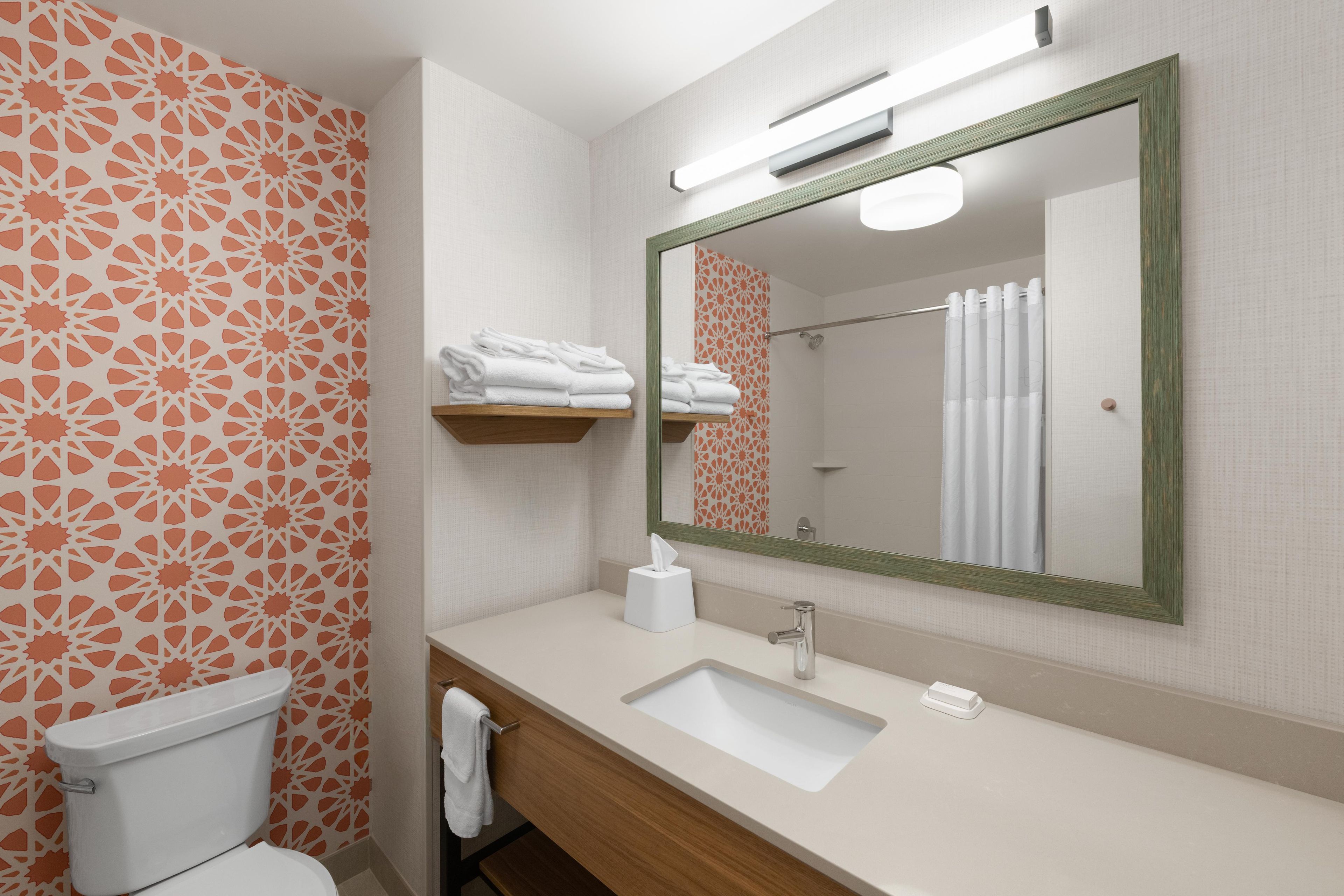 A bathroom with a toilet, sink, and mirror. There are towels on a shelf and a shower curtain.