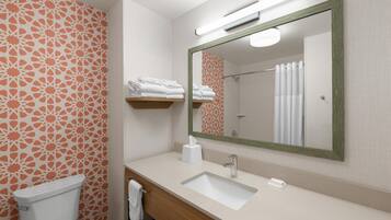 A bathroom with a toilet, sink, and mirror. There are towels on a shelf and a shower curtain.