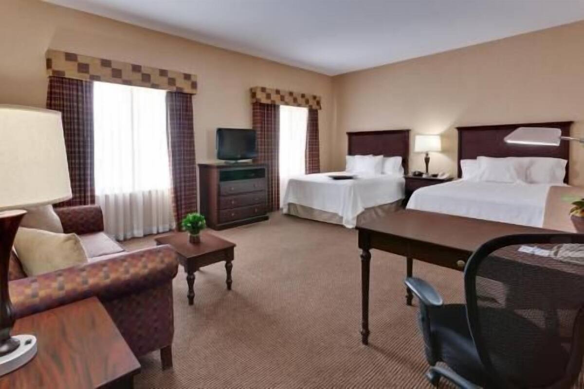 A hotel room with a bed, a desk, a chair, a TV, and a dresser.