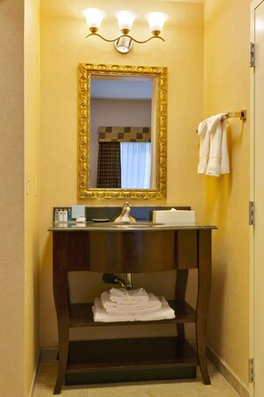 A bathroom with a golden-framed mirror, a sink with a faucet, and a towel rack with folded towels.