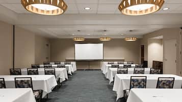 Un salón de conferencias con mesas, sillas, una pantalla de proyector e iluminación colgante.