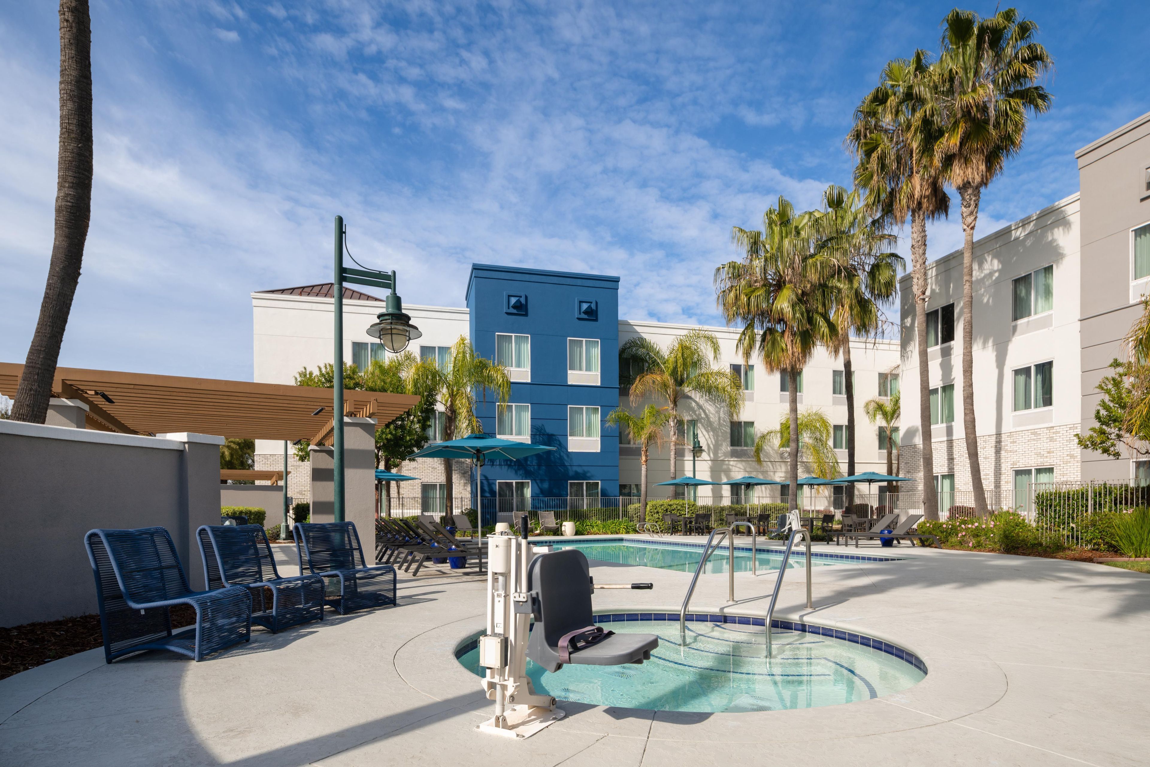 A pool area with lounge chairs, a hot tub, and a blue building in the background.