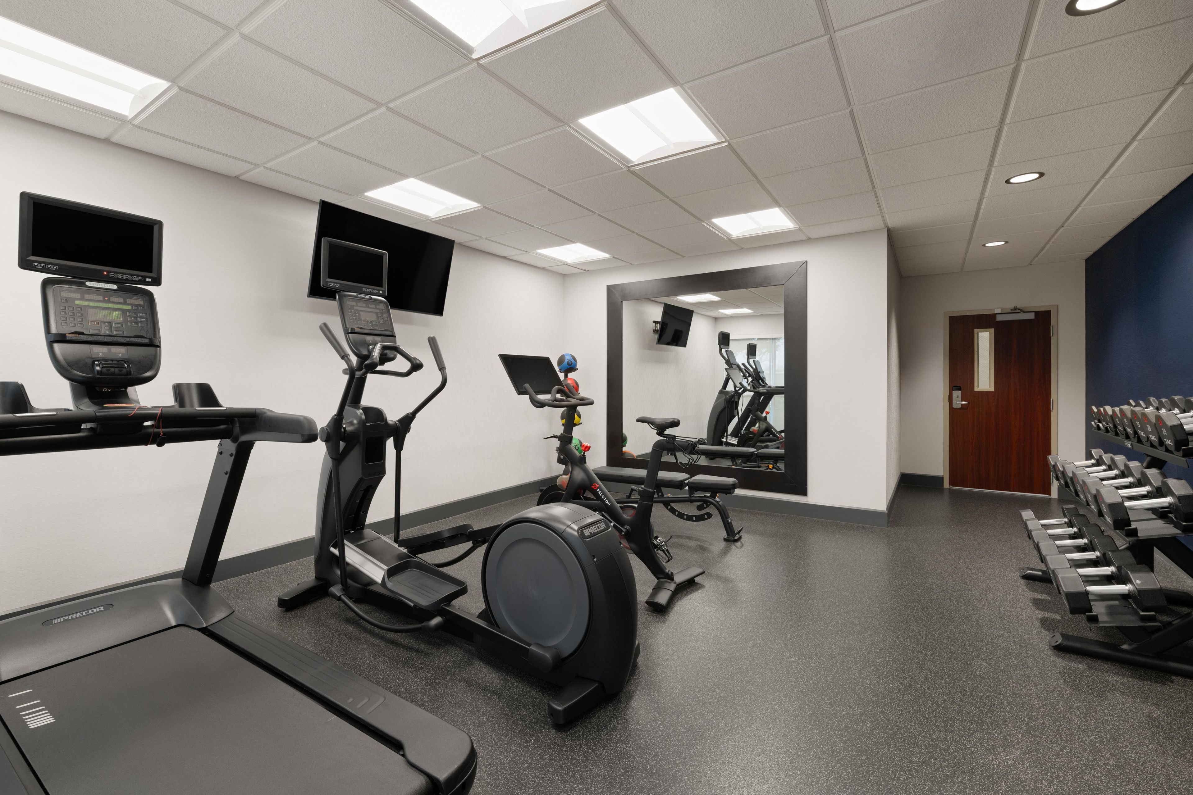 Ein Fitnessraum mit Trainingsgeräten, darunter Laufbänder und Ergometer, sowie einem an der Wand montierten Fernseher.