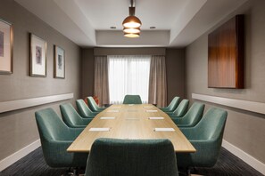 Una sala de conferencias con una larga mesa, sillas tapizadas en verde, una lámpara en el techo e imágenes enmarcadas en las paredes.