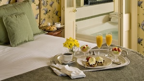 Habitación de hotel con cama, una mesita de noche con lámpara, una bandeja con alimentos para el desayuno y vista a una chimenea.